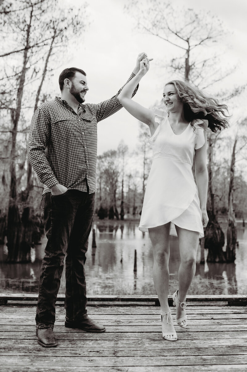 man and woman dance together on a dock at a lake  for engagement photos in little rock ar