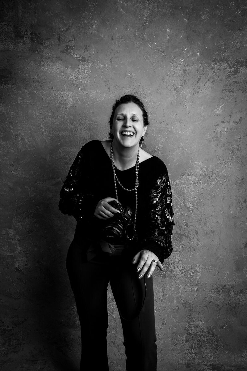 Black and white photo of Heidi cracking up holding her camera at the studio
