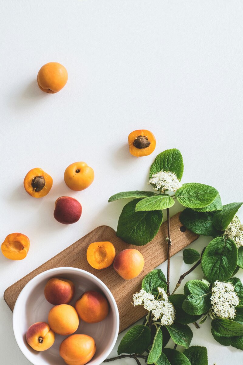Sliced peaches in a white bowl on a wooden cutting board next to a large plant