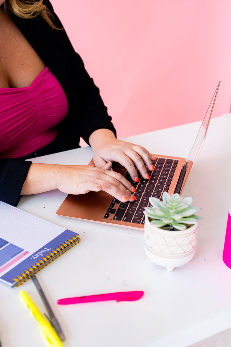 Jessi Cabanin desk with a notebook that  reads This way to Fabulous.  She is typing on a laptop.