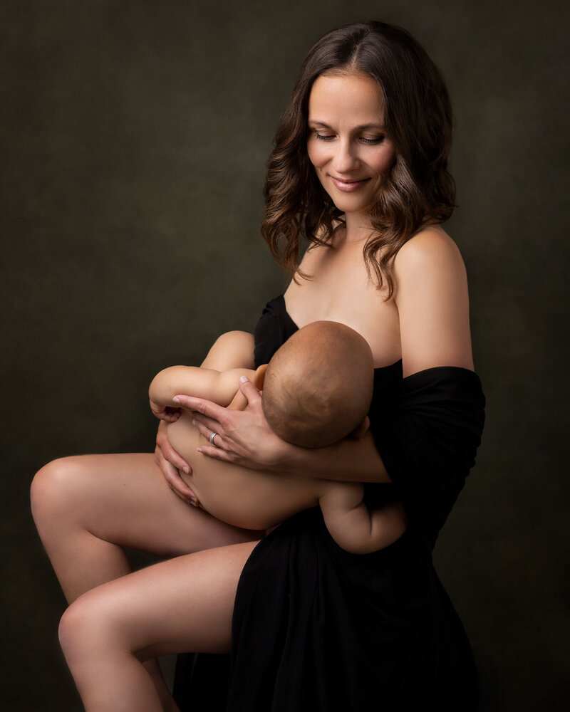 Breastfeeding mother wearing black dress smiling at her baby