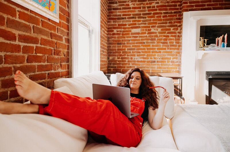 A woman laying on a couch with her legs up working on a laptop.