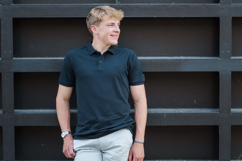 a guy in a navy polo shirt posing against a wall