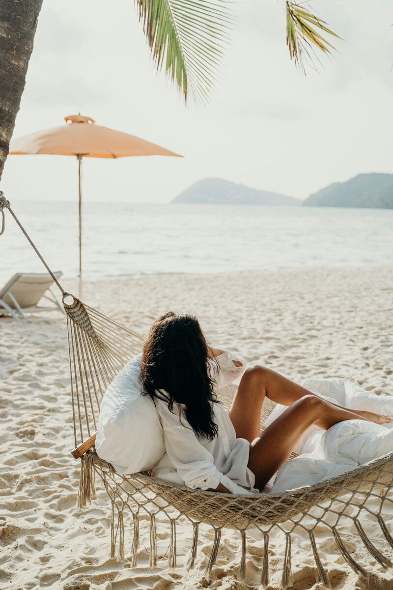 woman on a cozy hammock on the beach looking out into the ocean, feeling calm and relaxed
