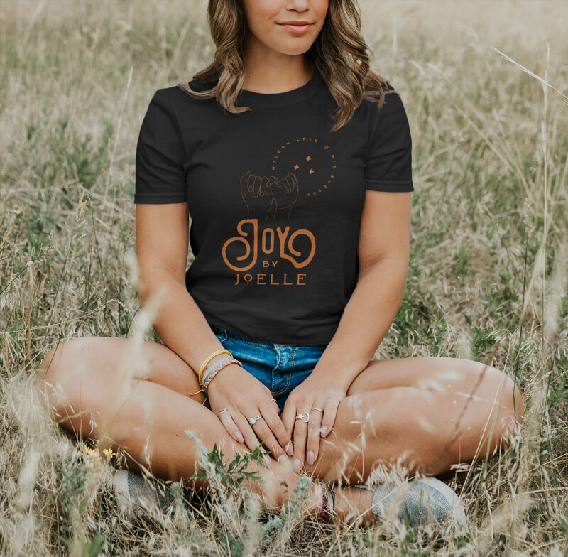 Woman sitting in a grassy field with black t-shirt and jean shorts.