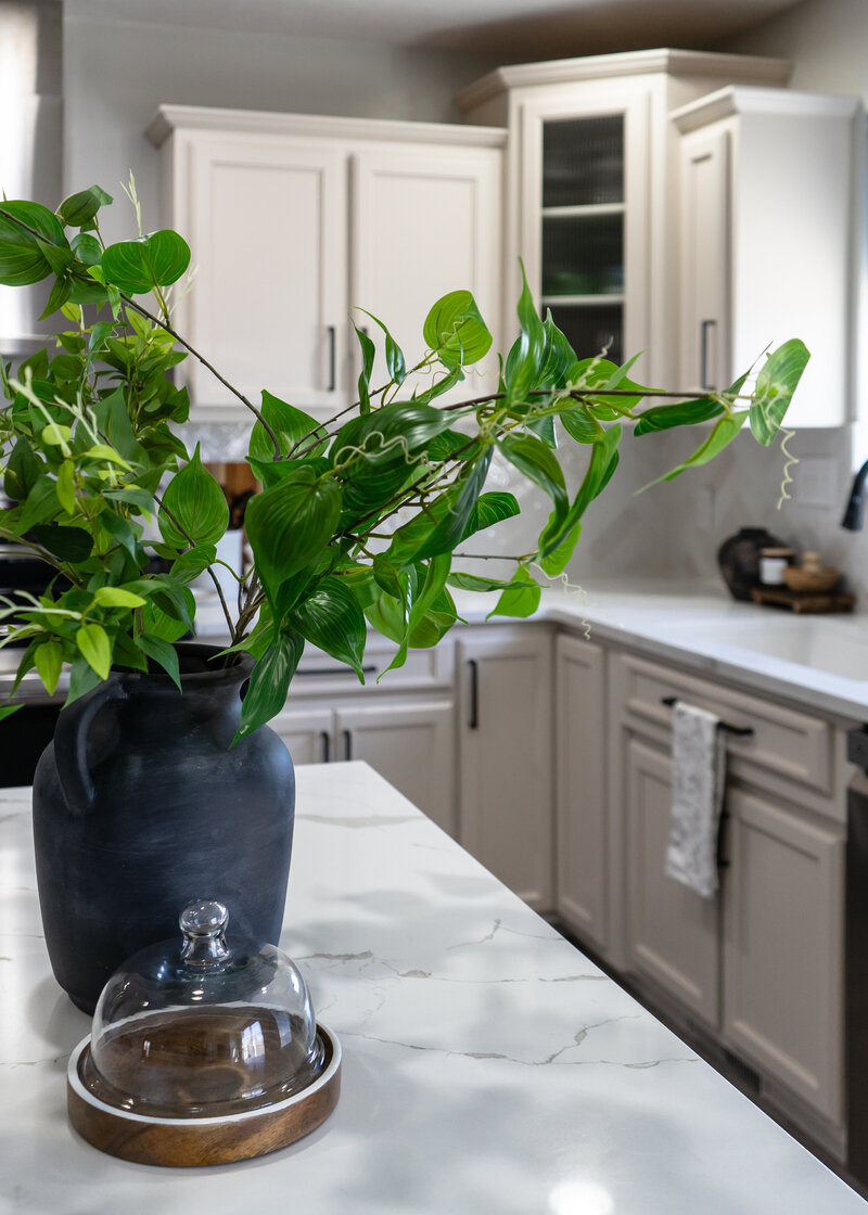 Close up view of a kitchen island with a black vase and faux greenery showcasing a beige white kitchen with quartz countertops.