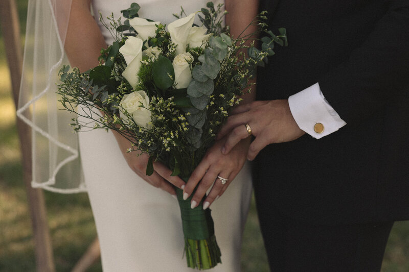 ose-up of a bride holding a lush bouquet of white roses and greenery, capturing the delicate details of her wedding day