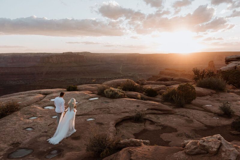 bride and groom walking through the desert towards the sunset in moab utah