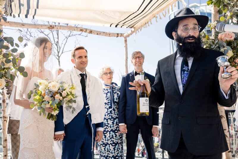 a jewish couple gets married under a huppah with their family. 
