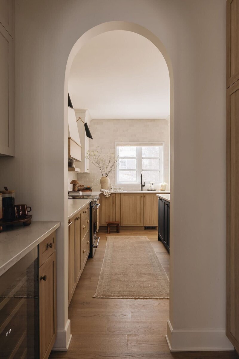 Montreal kitchen with arched doorway, black island, natural wood cabinetry, and soft neutral finishes – designed by Ingrid Interior Design.
