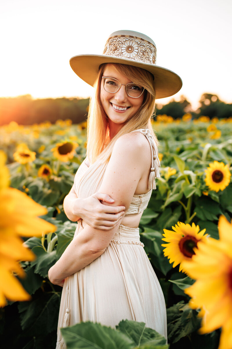 Stacy Lynn posing in a field of sunflowers wearing a cream dress and hat
