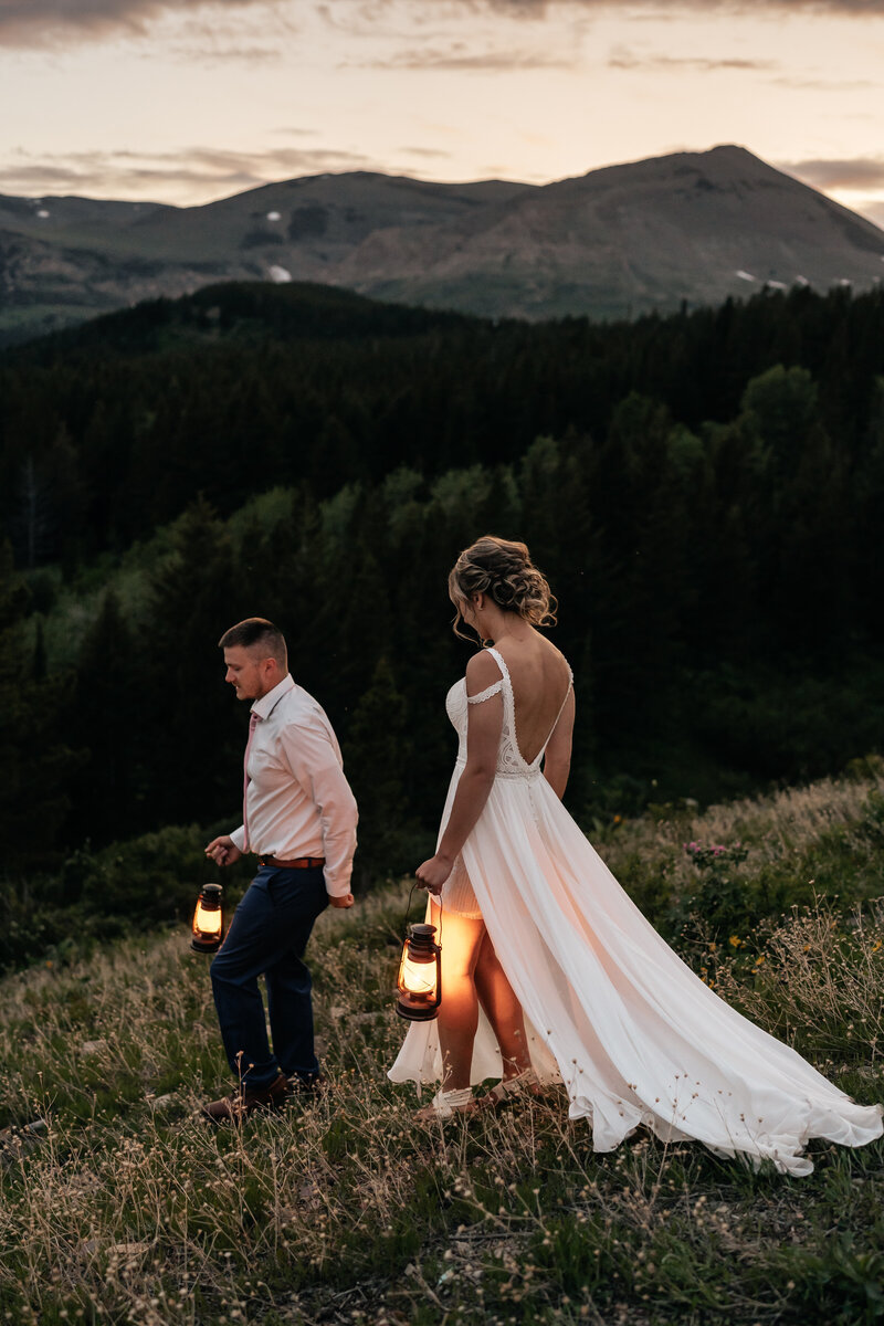 A couple holds lanterns and walks in front of a mountain landscape during their Montana Elopement.