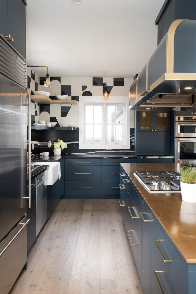 A modern kitchen design featuring deep blue cabinetry, stainless steel appliances, a black and white wall mural, and an island with a brass countertop and stove range