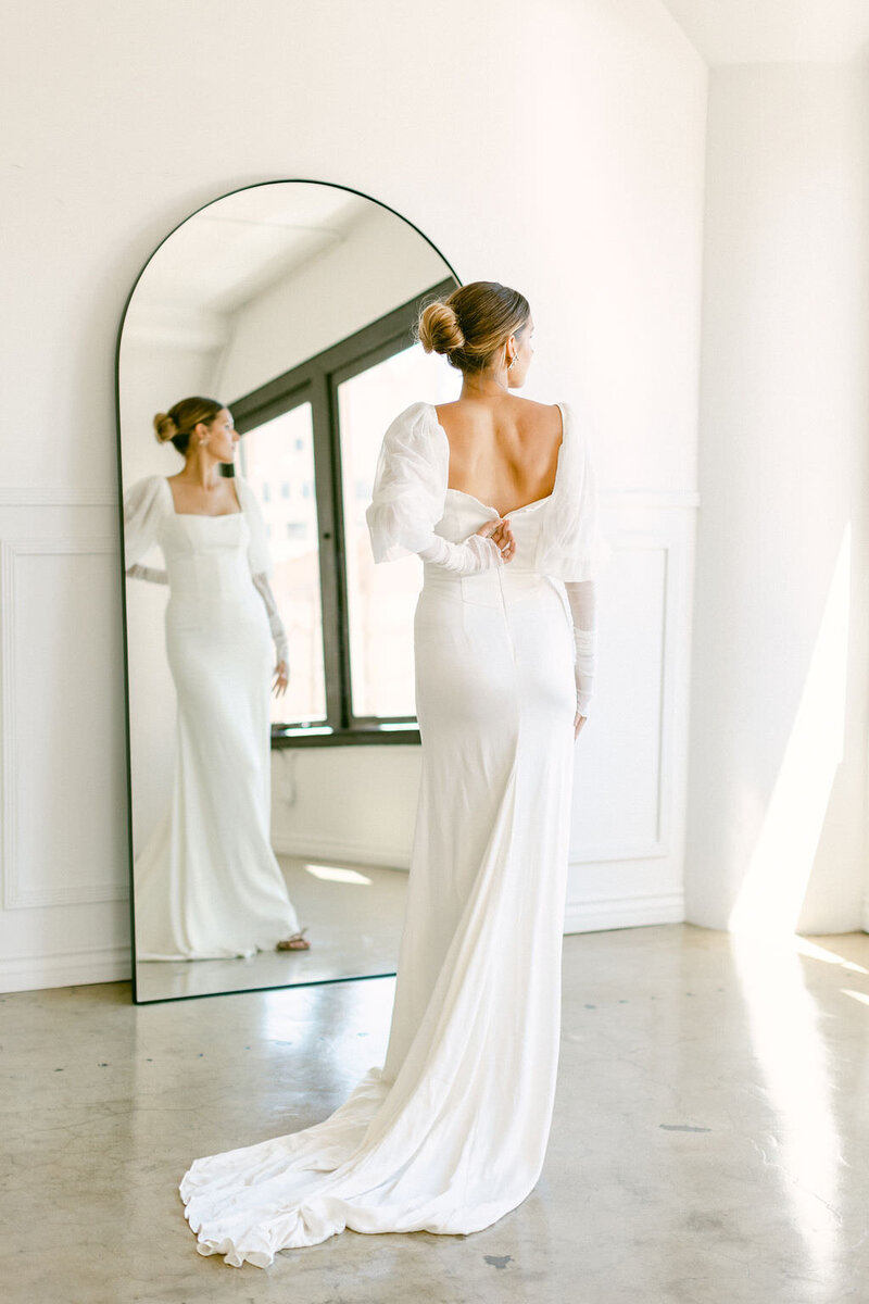 Modern bride zips up the back of her wedding gown and looks off to the side