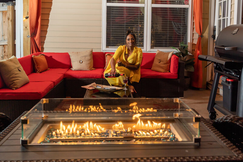 50th milestone birthday photoshoot woman wearing mustard colored romper sitting by outdoor firepit