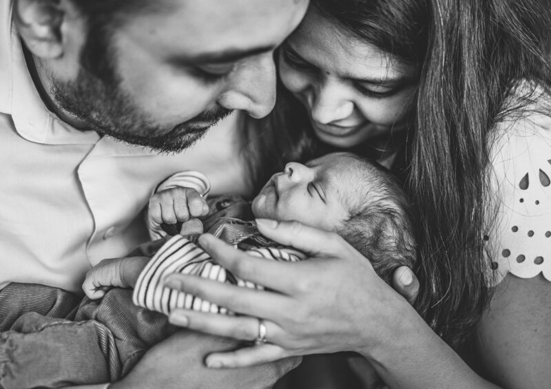 A black and white portrait of a mother and father holding and looking at their beautiful newborn taken with natural light in St. Louis, Missouri. 