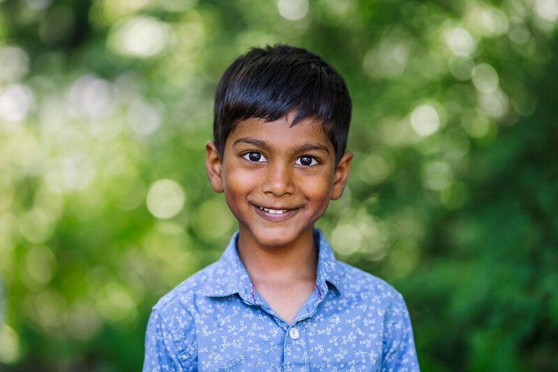 boy in a blue shirt with a nature background smiling at the camera