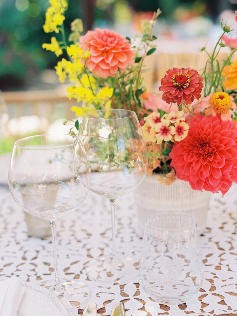 close up photo of two wine glasses with bright pink and yellow flowers surrounding on a wedding table setting at the holly farm in carmel ca