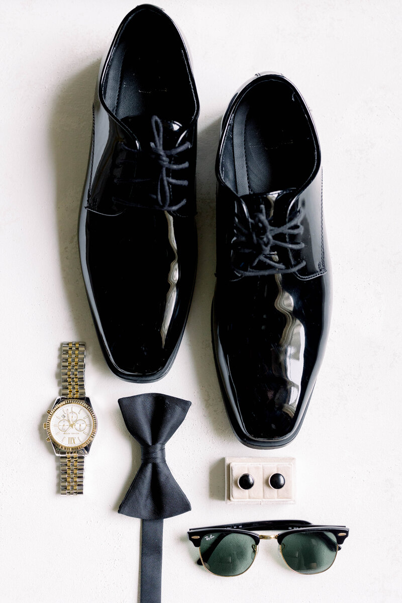 Wedding Videography in Newport, CT, RI, and beyond | The Corteses | Flat lay for groom with black shoes, a bow tie, sunglasses, and a watch