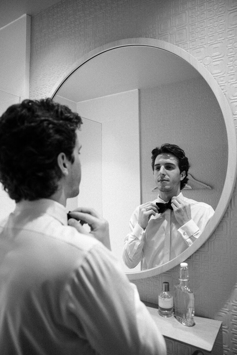 groom getting ready in front a mirror and fixing his bowtie