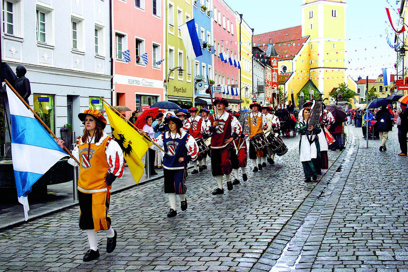 People marching in a parade with decorative clothing holding flags and instruments in Munich Germany