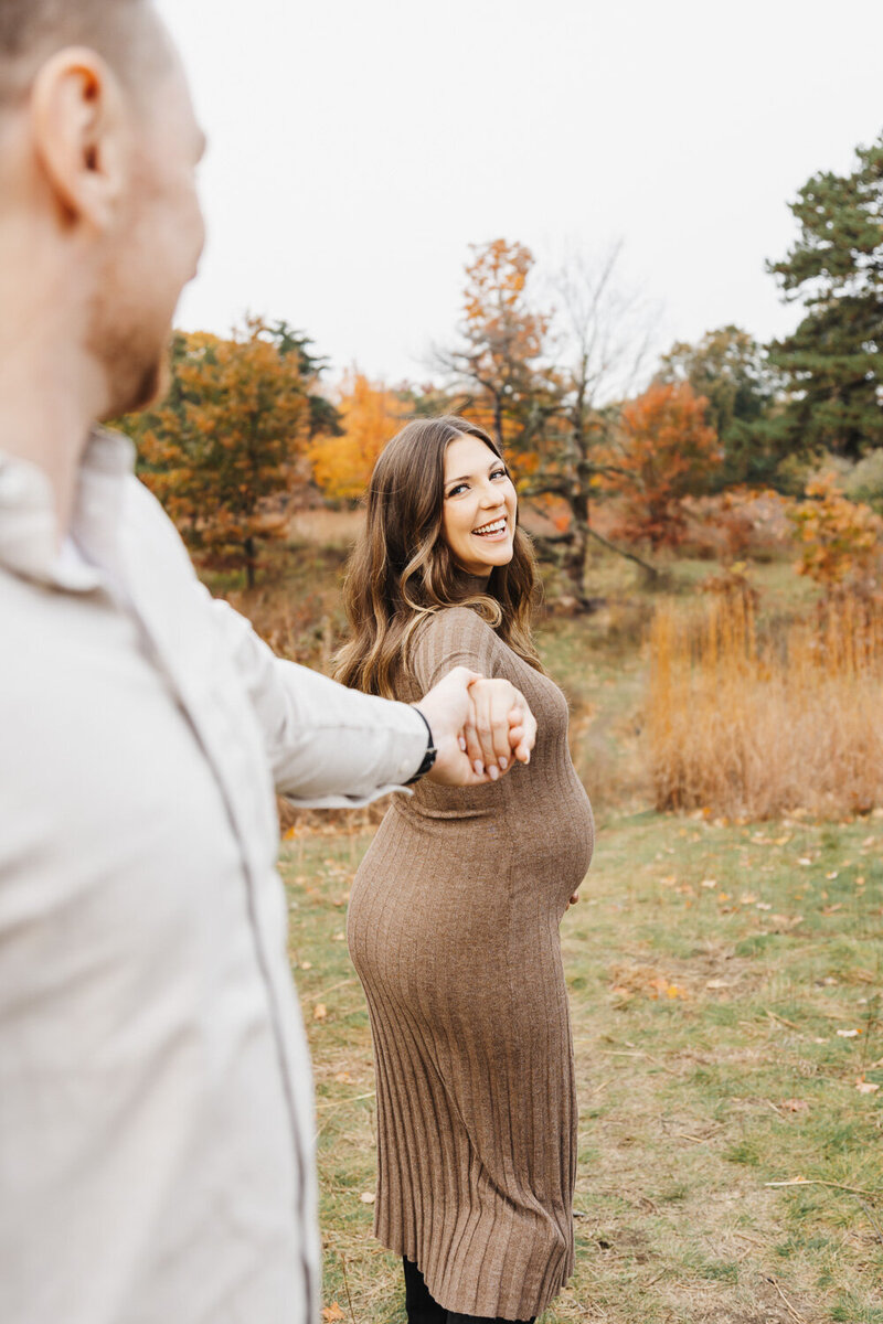 Beautiful pregnant woman  smiling back at her husband as she leads him on a walk in Toronto's High Park