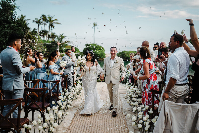 Happy couple walking down the aisle under a flower toss on a Mexico beach. 
