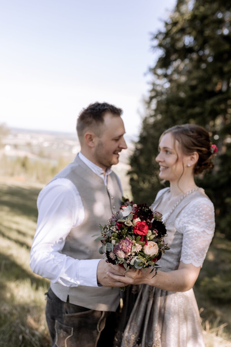 Mann und Frau stehen in Hochzeitstracht auf einer Wiese und halten den Brautstrauss