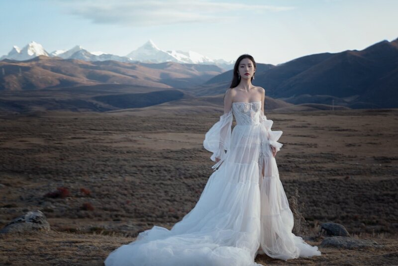 A beautiful woman wearing a couture bridal dress photographed in wild fields with snow capped mountains in the background.