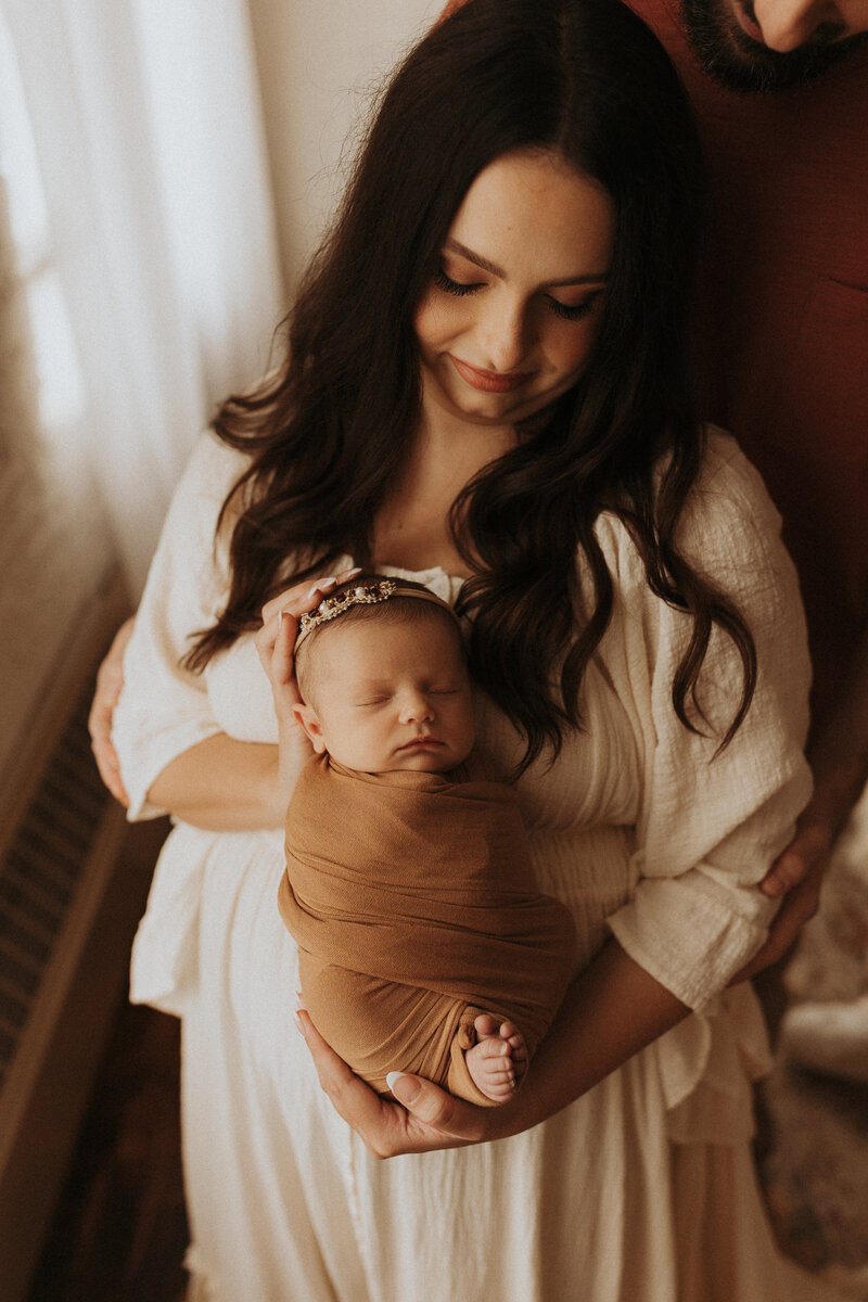 New mother holding her baby girl who is wrapped in a swaddle and wearing a flower crown.