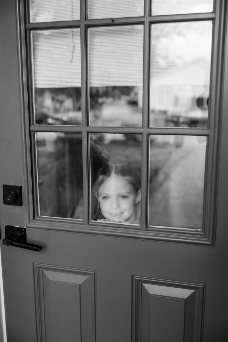 Flower girl in a black and white photo peeking through the window of a door by Orlando wedding photographer. 