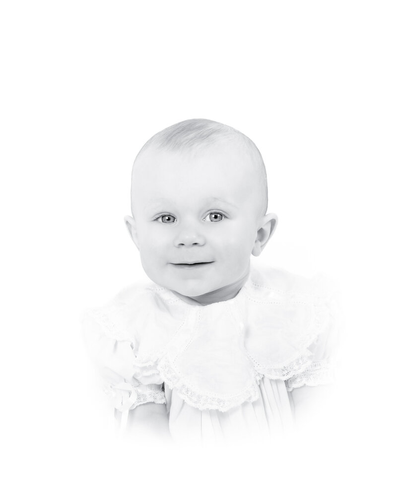 Black and white heirloom portrait of a smiling baby dressed in a classic white outfit with lace details. This timeless baby photography captures the innocence and joy of childhood, created by a Birmingham newborn photographer specializing in elegant, light-filled portraits.