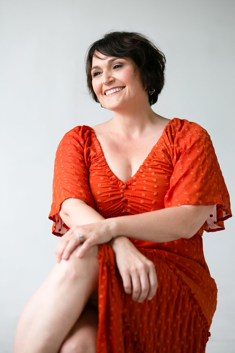 A woman in an orange dress smiling with her legs crossed