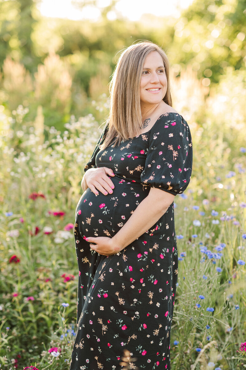 mother holding belly in wildflower field wearing a black dress with flowers  by york pa photographer maternity