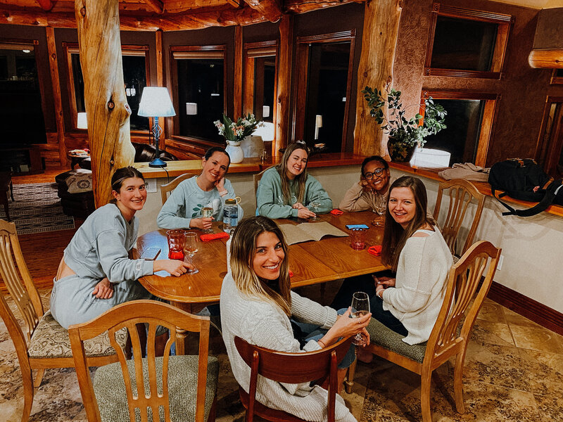 A group of women sit around a dining table smiling. 