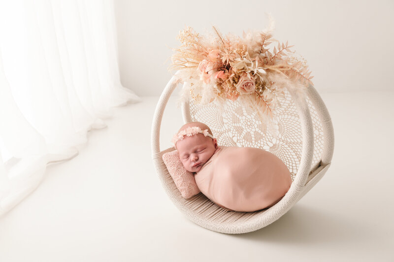 geposeerde newborn baby op kussen in witte minimalistische setting op een dromenvanger met bloemen