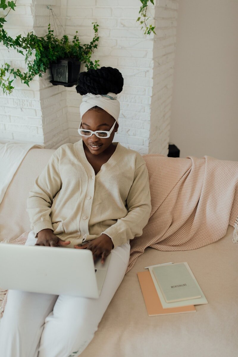 An image of a Black woman sitting on a couch with a laptop on her lap.