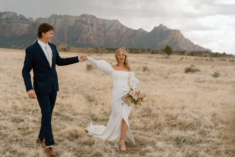 groom twirling his bride with an epic view behind them near Zion National Park on an overcast day