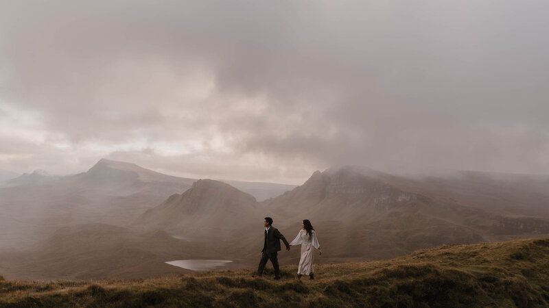 Couple walking hand in hand across the Isle of Skye’s Quiraing landscape during a Scottish elopement, photographed in a cinematic fine art style by wedding photographer Aly Robinson.