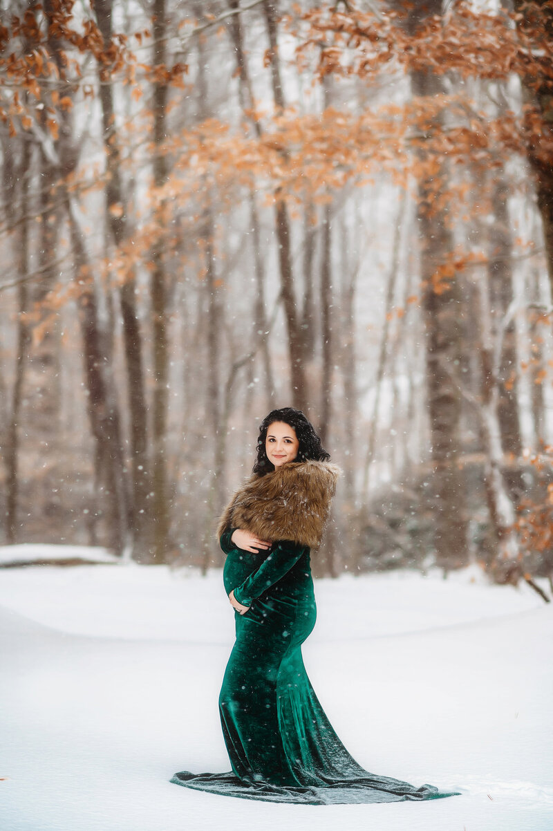 Pregnant woman cradles her bump during a snowy maternity portrait session in Asheville, NC.