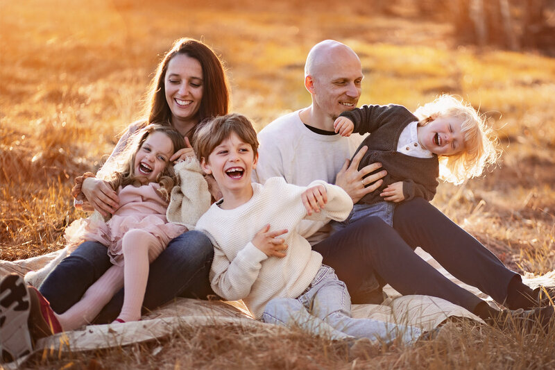 familj som skrattar och kittlar varandra i solnedgången