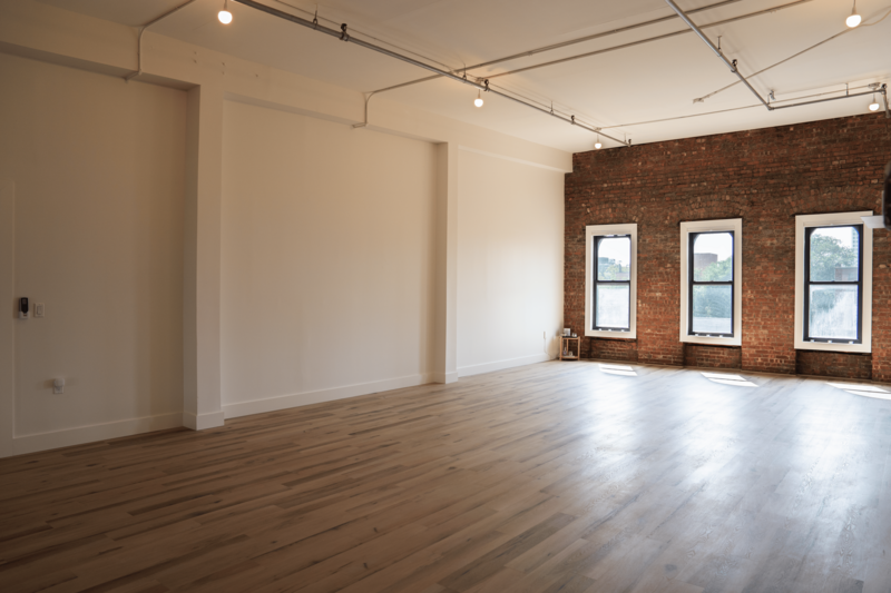 Natural  lit studio space for yoga, wellness and creative workshops in Brooklyn, NY with fresh wood flooring, exposed brick walls and several large windows with a view. 
