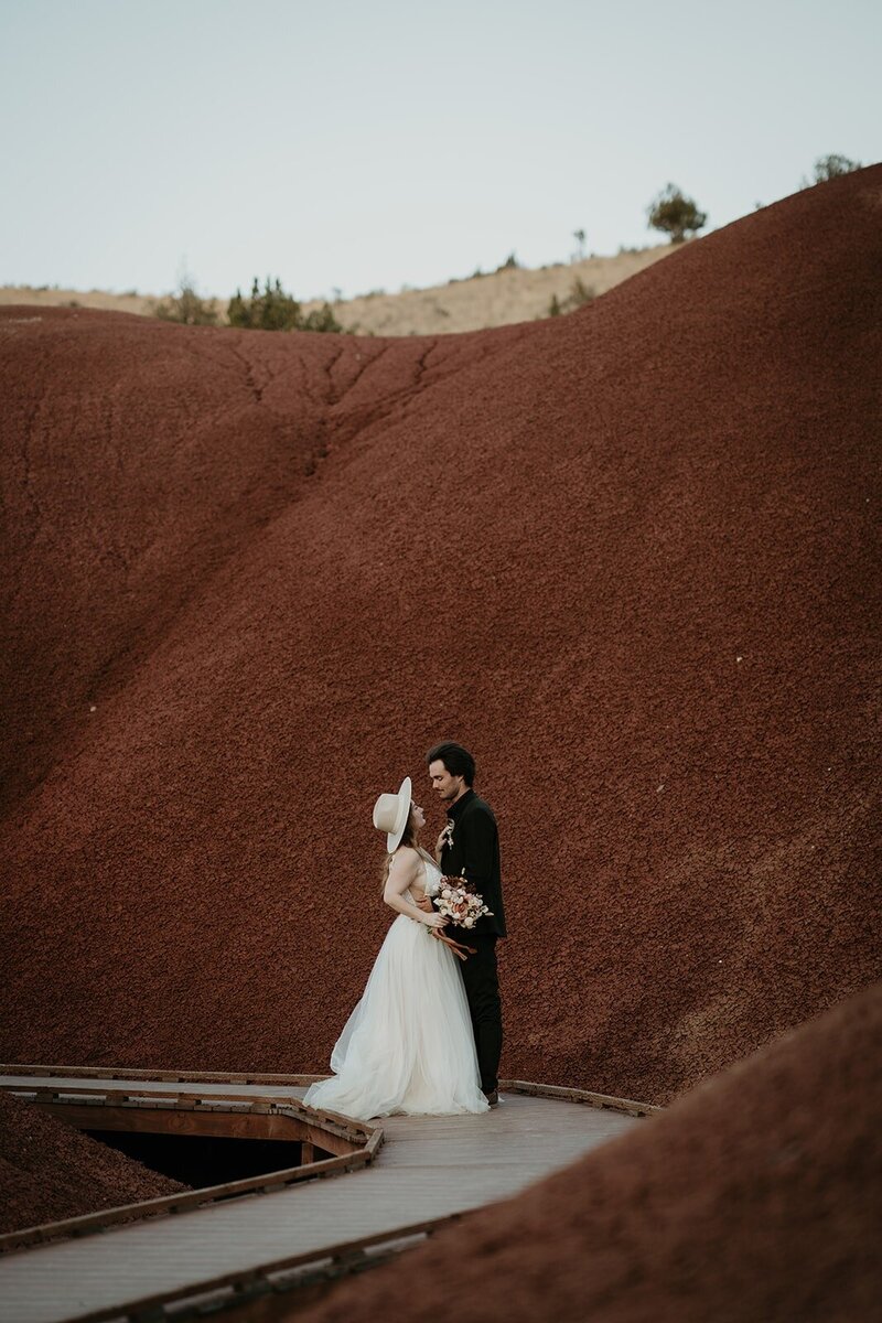 Bride and groom stand face to face on a wood boardwalk during their Oregon elopement photography session at Painted Hills