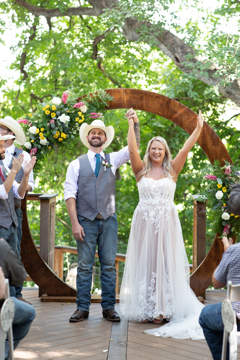 A bride and groom stand in front of a wooden arch during their Austin wedding ceremony.