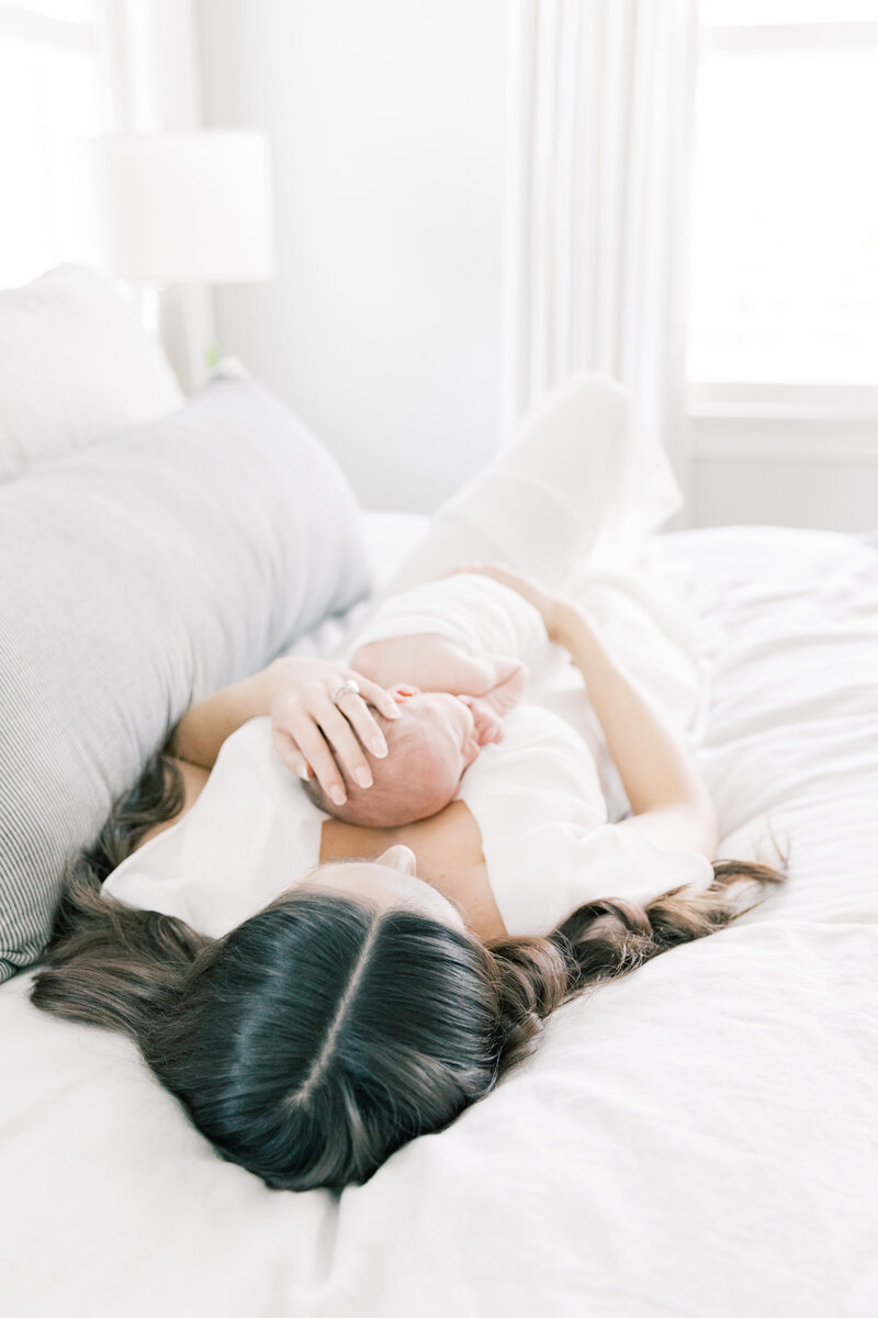 Newborn baby lying on a white bed with natural light during a lifestyle session.