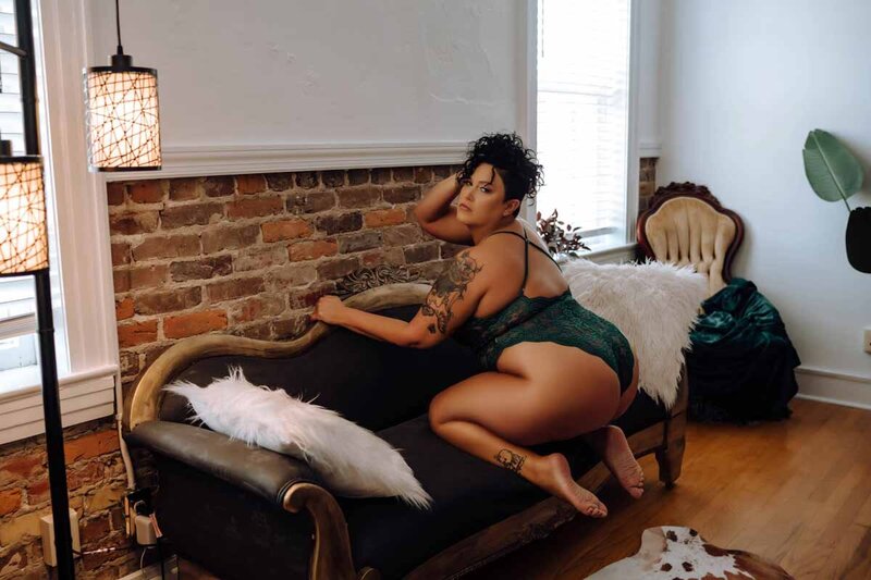 Woman posed kneeling on couch for dark and sultry boudoir photoshoot