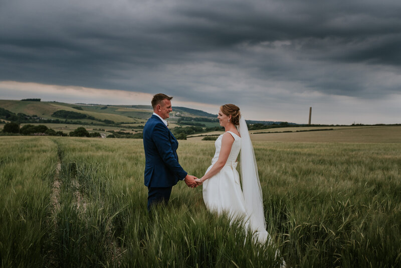Bride and groom holding hands in field for portrait