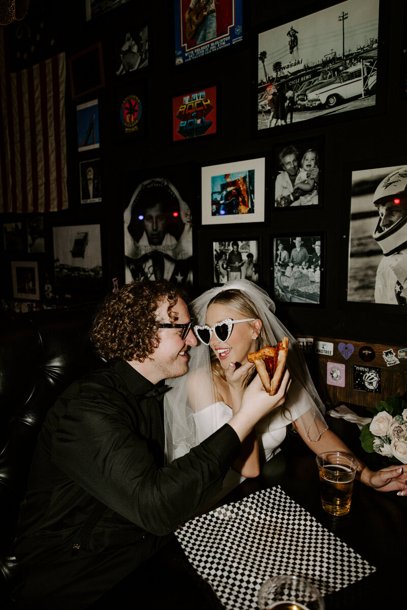 A couple smiles at one another while holding a slice of pizza