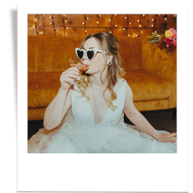 Close up of Bride sipping glass of champagne with heart-shaped sunglasses on