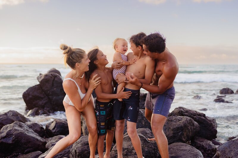 large family portrait with siblings looking at young baby and laughing